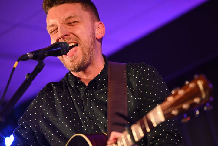 Close-up of Tom Ryder singing under purple stage light