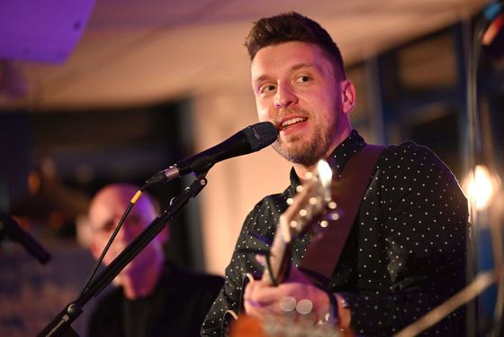 Warm close-up of Tom Ryder singing in a polka-dot shirt at a wedding