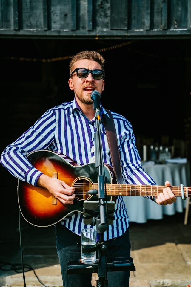 Tom Ryder playing indoors with the wedding breakfast tables laid behind him.