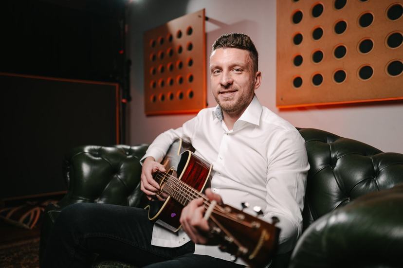 Tom Ryder with his guitar, smiling.